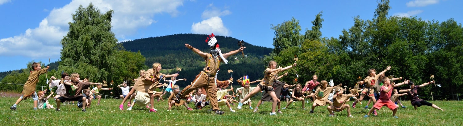 Děti v kostýmech tančí indiánský tanec na louce